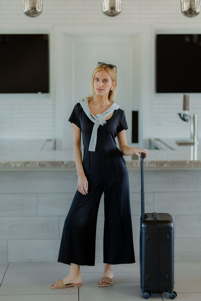Woman wearing a black tailored short sleeve jumpsuit with wide cropped legs, styled with sandals, from The Pink Doxie Boutique.