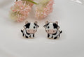 Cow printed post earrings with gold trim displayed on a white background from The Pink Doxie Boutique.