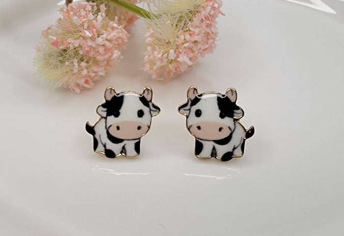 Cow printed post earrings with gold trim displayed on a white background from The Pink Doxie Boutique.