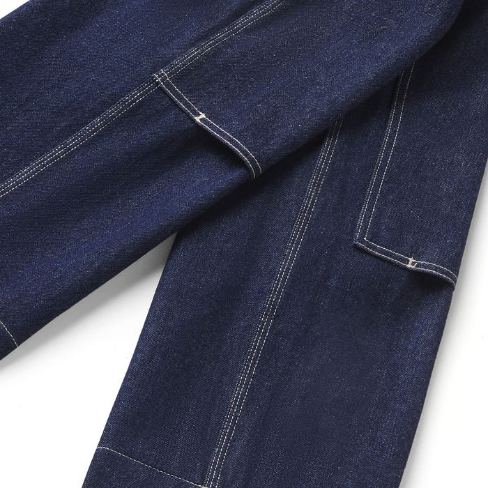 Close-up of dark indigo denim fabric with white contrast stitching, showing part of a pocket and seam detail on a white background.
