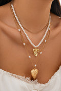 Gold layered necklace with pearls, gold bow charm, and engraved heart pendant displayed on white bust — elegant jewelry from The Pink Doxie Boutique