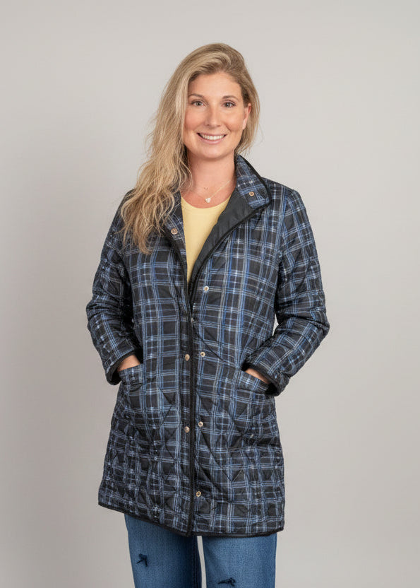 Woman wearing a plaid quilted puff jacket with zip front and pockets styled with jeans inside The Pink Doxie Boutique.