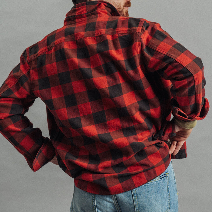 A man wearing a red and black buffalo plaid flannel shirt, shown from the back, paired with blue jeans against a plain gray studio background.