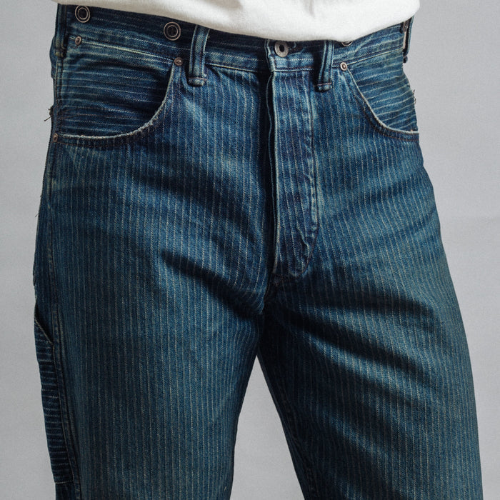 Close-up of a person wearing dark blue denim jeans with a white t-shirt tucked in, against a plain gray background.
