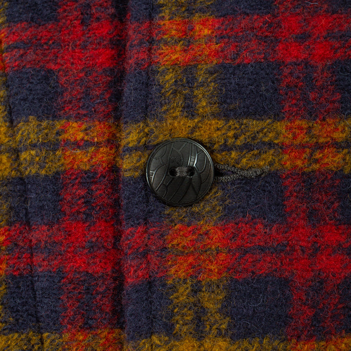 Close-up of a textured plaid fabric with red, navy, and mustard yellow stripes, featuring a single black button.